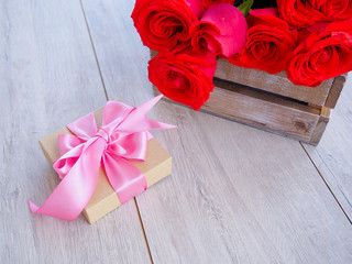 Valentine background of gift box with ribbon and bow and bunch of red roses on wood. Space for copy.