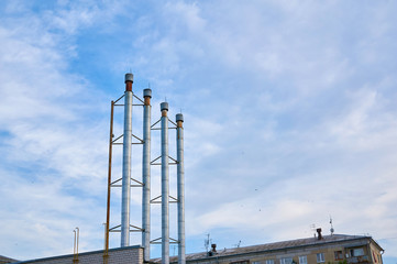Four pipes from the boiler room against the blue sky with clouds.