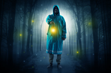 Man in raincoat coming from dark forest with glowing lantern in his hand concept
