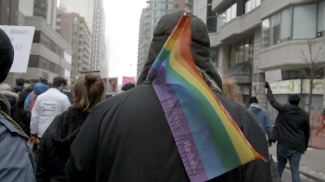 medium slomo clip behind marching protester in crowd with pride rainbow flag