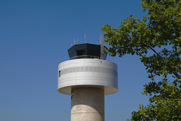 Tower eines Flughafens vor einem blauen Himmel mit einem gr&uuml;nen Busch