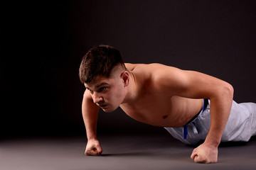 Fototapeta na wymiar An athlete doing push-ups on fists on the gray background in the studio