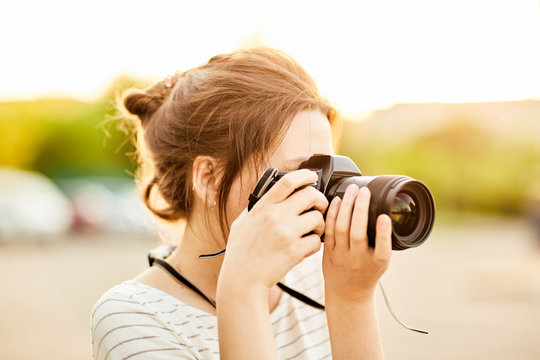 young girl taking pictures on camera in a summer Park at sunset