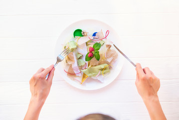 Top view female hands holding knife and fork over the plate with unreal salad from recycle waste,...