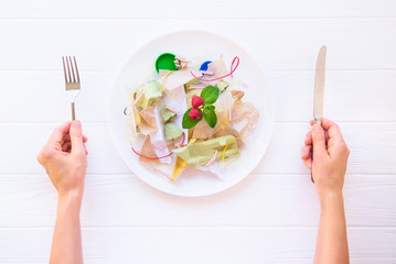 Top view female hands holding knife and fork over the plate with unreal salad from recycle waste,...