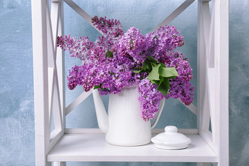 Pot with blossoming lilac on shelf against color background. Spring flowers