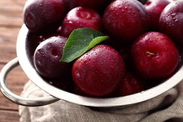 Colander with ripe juicy plums on table, closeup