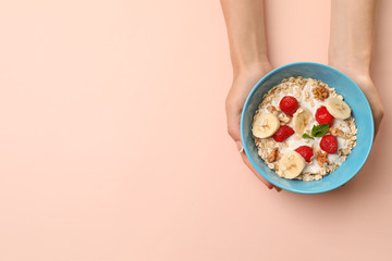 Woman holding bowl with oatmeal and fresh fruits on color background