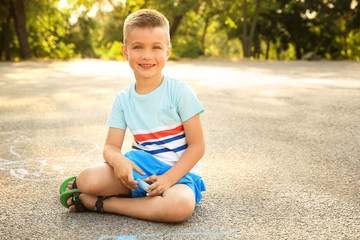 Cute little boy drawing with chalk, outdoors