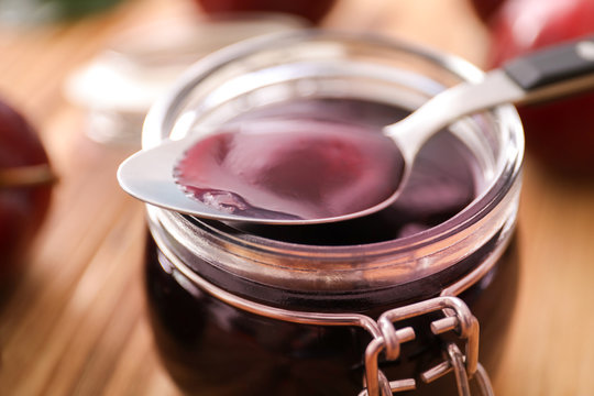 Spoon and jar with tasty plum jam on table