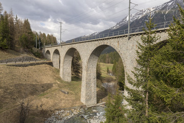 Railway bridge over the river Vallember in Switzerland with snowy mountains in background