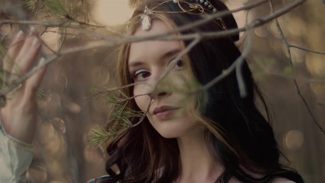 Young elf princess is strolling in autumn woodland. She is looking at camera through branch of spruce, close-up of her pretty face