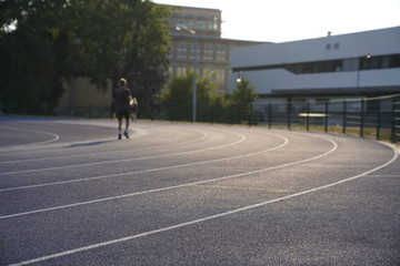 Blue outdoor stadium running track with white dividing lines and a blurred person running on the background