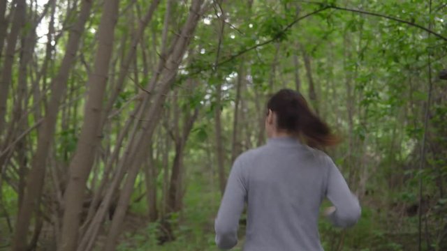 Young woman running through the woods, looking back.