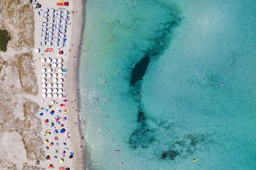 Aerial view of an emerald and transparent Mediterranean sea with a white beach full of beach umbrellas and tourists who relax and take a bath. Costa Smeralda, Sardinia, Italy.