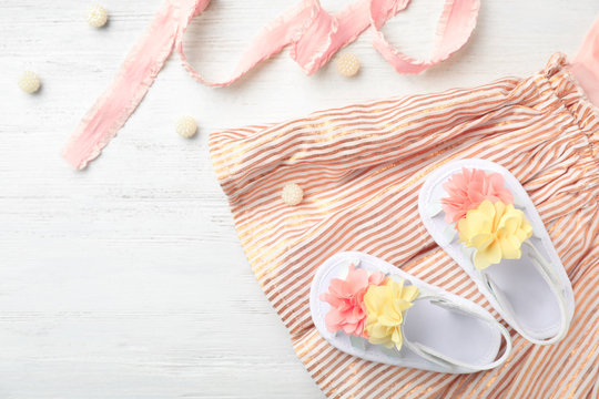 Pair of cute baby sandals and clothes on table, top view
