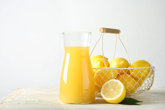 Basket with ripe lemons and glass jug of fresh juice on table