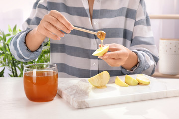 Woman pouring honey onto sliced apple at table