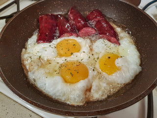 Appetizing smoked sausages and eggs for breakfast are fried in a frying pan in oil
