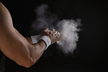 Young man applying chalk powder on hands against dark background