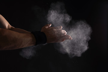 Obraz na płótnie Canvas Young man applying chalk powder on hands against dark background