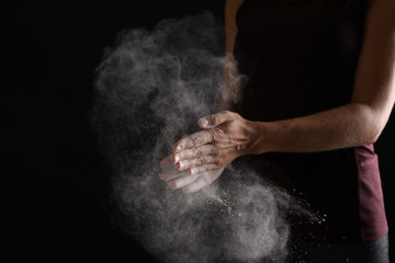 Fototapeta na wymiar Young woman applying chalk powder on hands against dark background