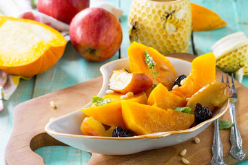 Pumpkin baked with apples, prunes and spices in a bowl on a wooden table.