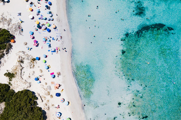 Fototapeta na wymiar Aerial view of an emerald and transparent Mediterranean sea with a white beach full of beach umbrellas and tourists who relax and take a bath. Costa Smeralda, Sardinia, Italy.