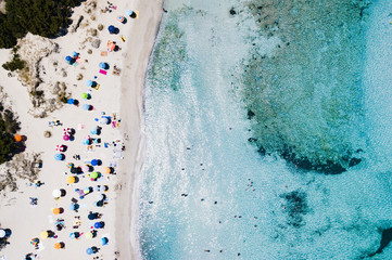Fototapeta na wymiar Aerial view of an emerald and transparent Mediterranean sea with a white beach full of beach umbrellas and tourists who relax and take a bath. Costa Smeralda, Sardinia, Italy.