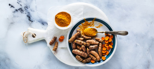 banner of roots of turmeric and powder from it on a white marble board and table. healthy natural supplements, spices for cooking