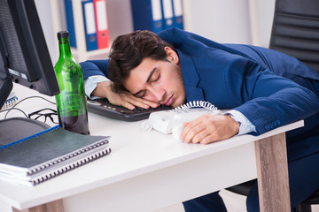 Young businessman employee drinking in the office at desk