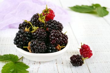 Delicious ripe blackberries in a ceramic bowl on a white wooden background.