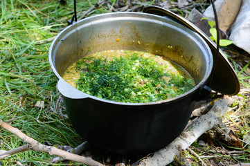 Delicious porridge cous cous with meat, vegetables and fresh herbs in a pot cooking on the nature.