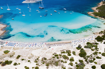 Aerial view of an emerald and transparent mediterranean sea with a white beach and some yachts....