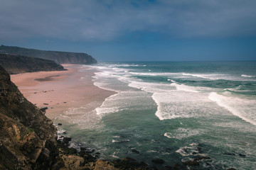 View of the Guincho beach near Atlantic coast. Surfer on the ocean coast with surfboard. Landscape of sunny day, blue sky and a mountain in distance. Cascais. Portugal.