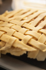 Close shot of raw strips of pastry in an unfinished lattice on a homemade apple pie.  Vertical image with shallow depth of field.
