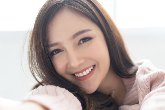 Closeup Portrait Of Inspired Caucasian Asian Lady Wearing Knitted Sweater Pink Cold Smiling And Taking Selfie At Her Home.Concept Woman Lifestyle And Winter.