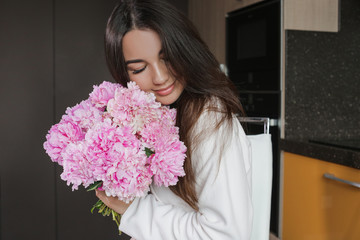 joyful girl in the kitchen with a bouquet of pink flowers peonies, joy and smile