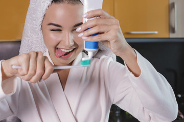 naughty young beautiful girl with a towel on her head brushing her teeth. squeezing toothpaste