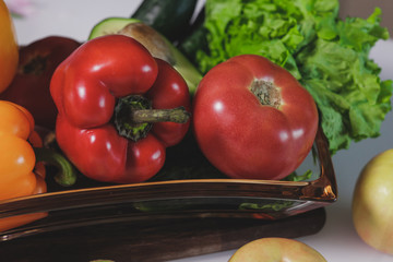 Top view of vegetables in plates prepared for slicing on a wooden board. There are sweet peppers, avocado and lettuce in a glass plate.