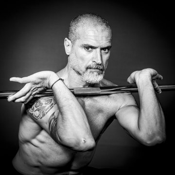 A man 50 Y is holding an outrigger raising the weights. Black background.
