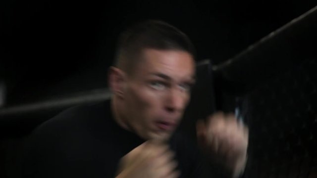 muscular fighter boxing in a black cage at gym.