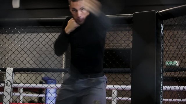 muscular fighter boxing in a black cage at gym.