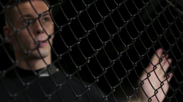 Exhausted Muscular fighter in Sweat Tries to Catch a Breath in a cage, close-up