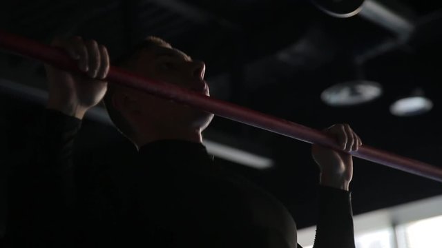 Man doing pull-ups in gym, black background, close-up