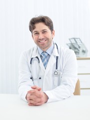 Handsome young doctor in white coat is looking at camera and smiling while standing in office
