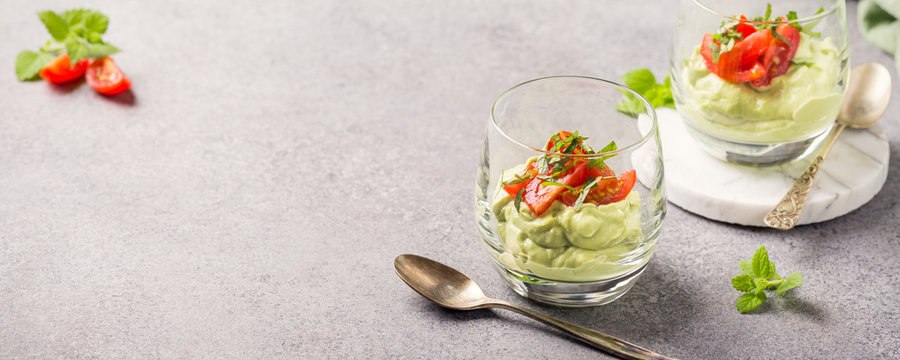 Fresh guacamole sauce from raw avocado with cherry tomatoes in glasses. Healthy vegetarian food concept with copy space.
