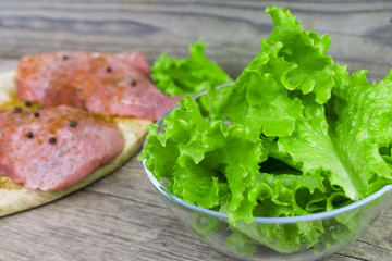 Raw meat with spices and salad leaves in a glass bowl on an old vintage wooden background