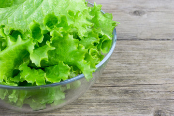 Fresh green lettuce leaves in a glass bowl on an old wooden background closeup