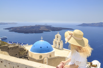 Blonde woman watching view of Santorini near three bells of Fira church in Fira, Santorini, Greece